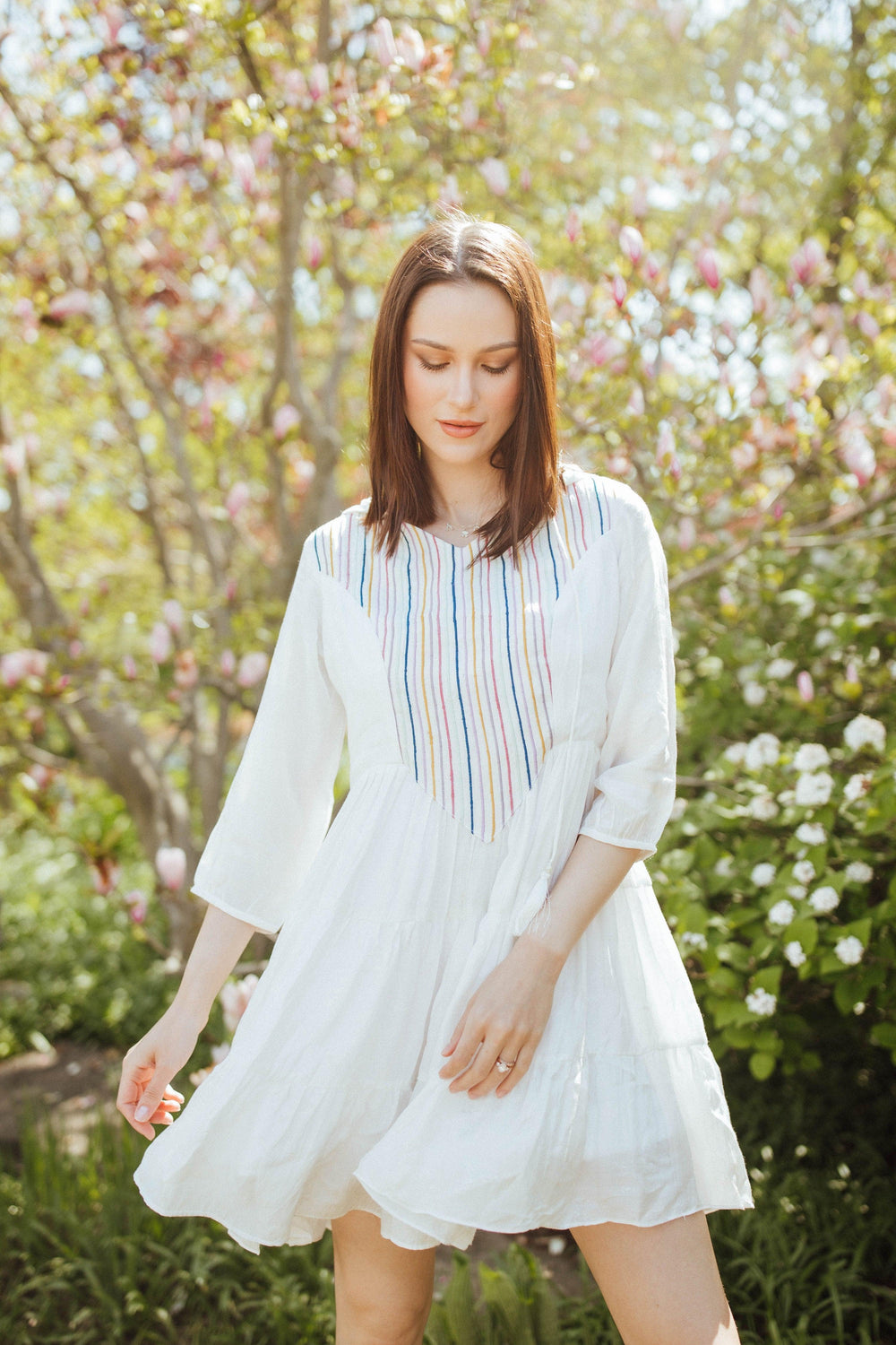 White tiered mini dress with colorful resham embroidery, 3/4 sleeves, and a hood, worn outdoors.