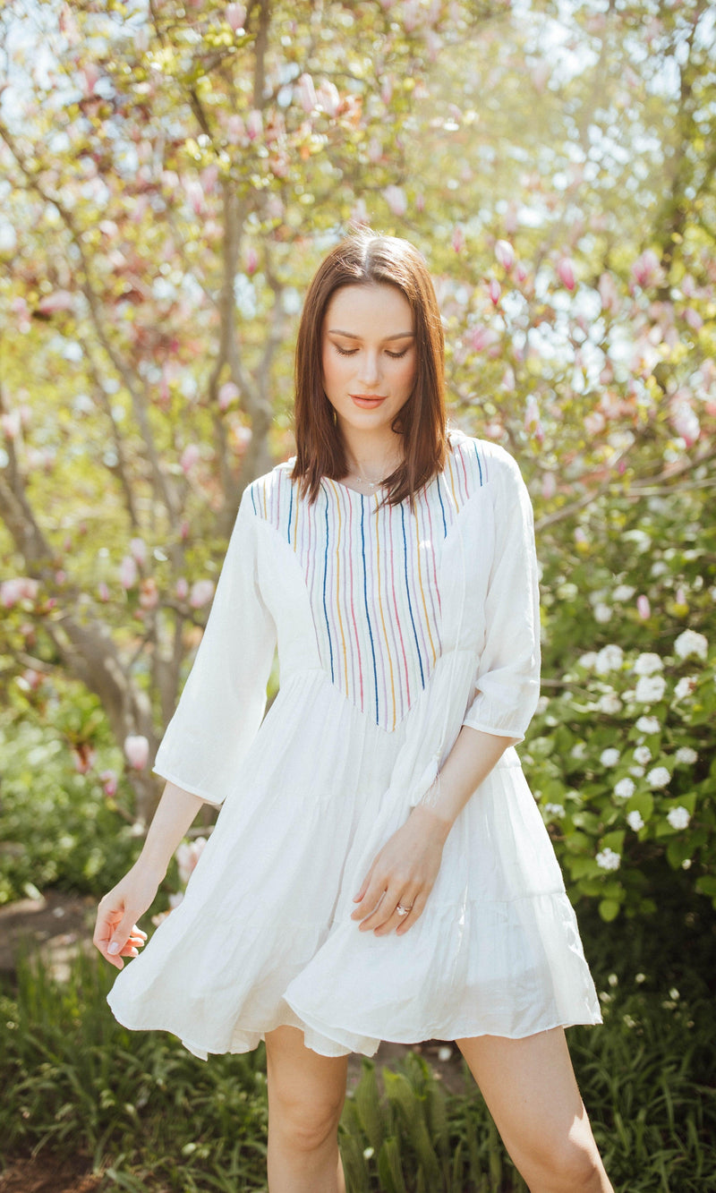 White tiered mini dress with colorful resham embroidery, 3/4 sleeves, and a hood, worn outdoors.