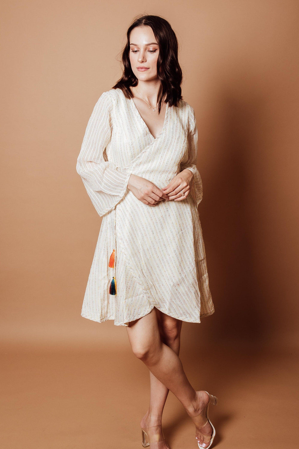 Off-white georgette wrap dress with subtle patterns, full sleeves, and colorful tassel details.