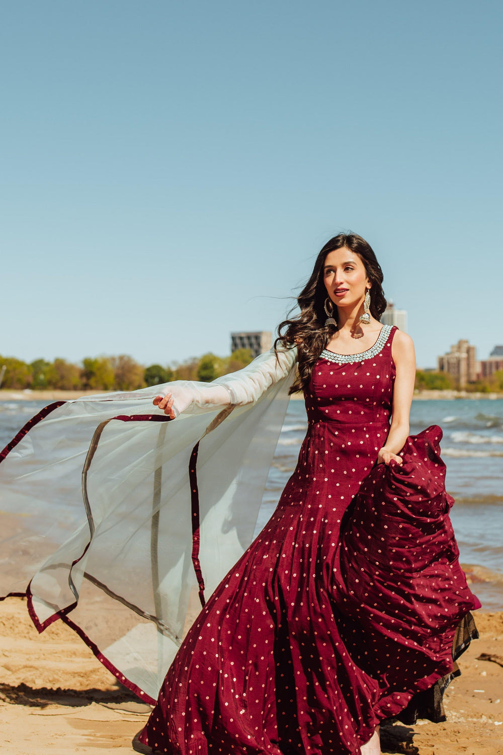 Wine silk a-line gown with resham and mirror embroidery, paired with a flowing net drape on a beach.