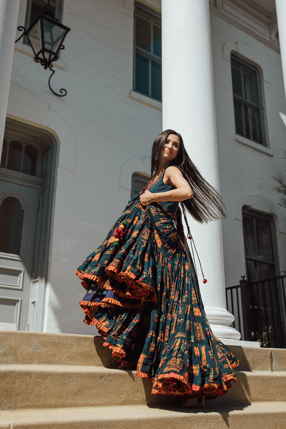 Woman in a full flare blue Chaniya Choli with vibrant ethnic prints, twirling on steps.