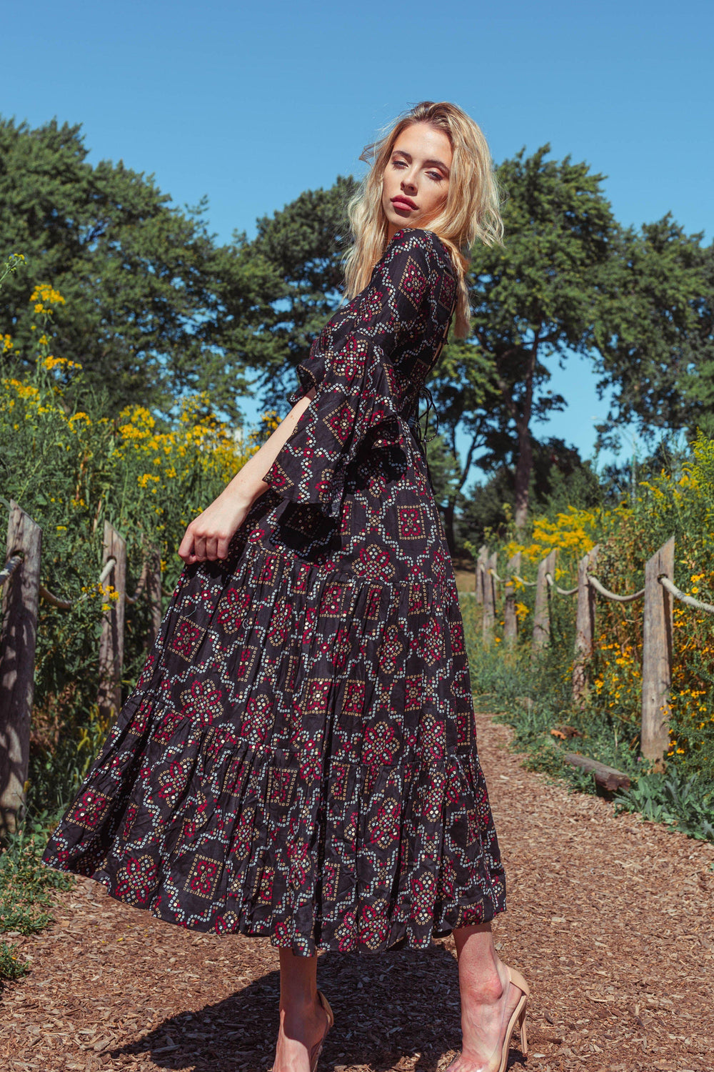 Woman in a black tiered midi dress with red and white geometric patterns, ruffle sleeves, and a string tie back.