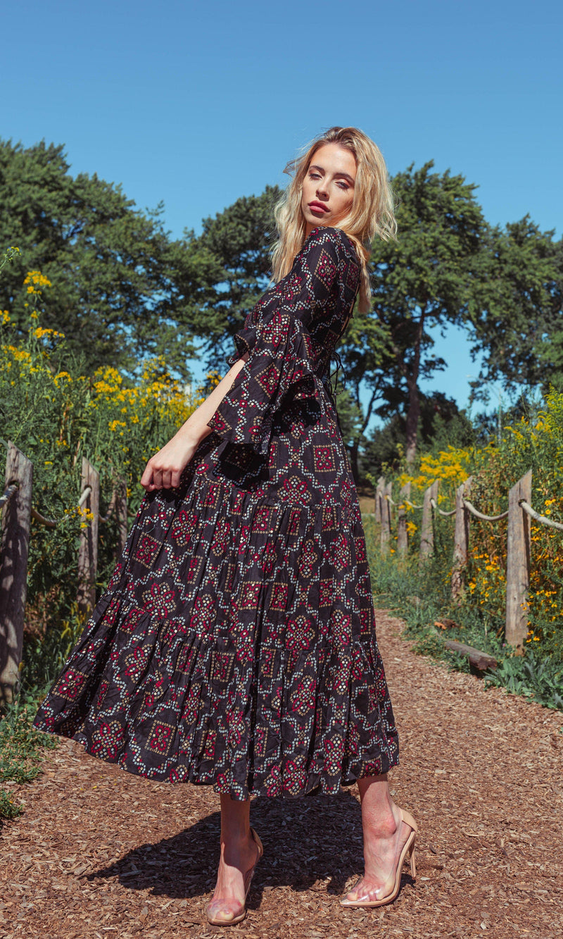 Woman in a black tiered midi dress with red and white geometric patterns, ruffle sleeves, and a string tie back.
