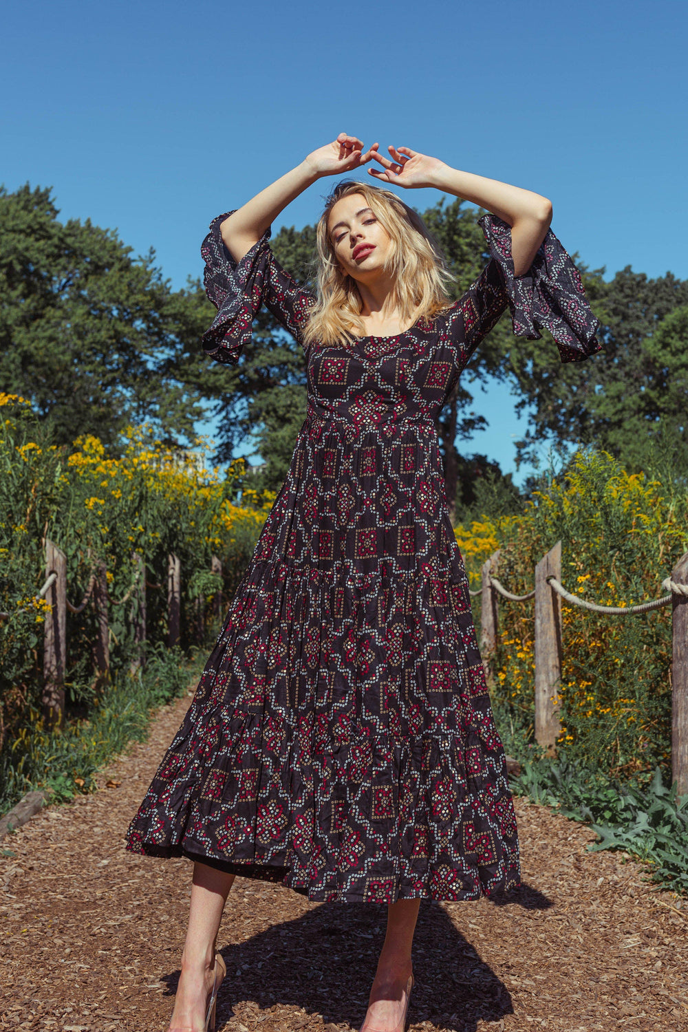 Boho-inspired midi dress with ruffle sleeves, black and red geometric print, tiered skirt, and embroidered bodice.