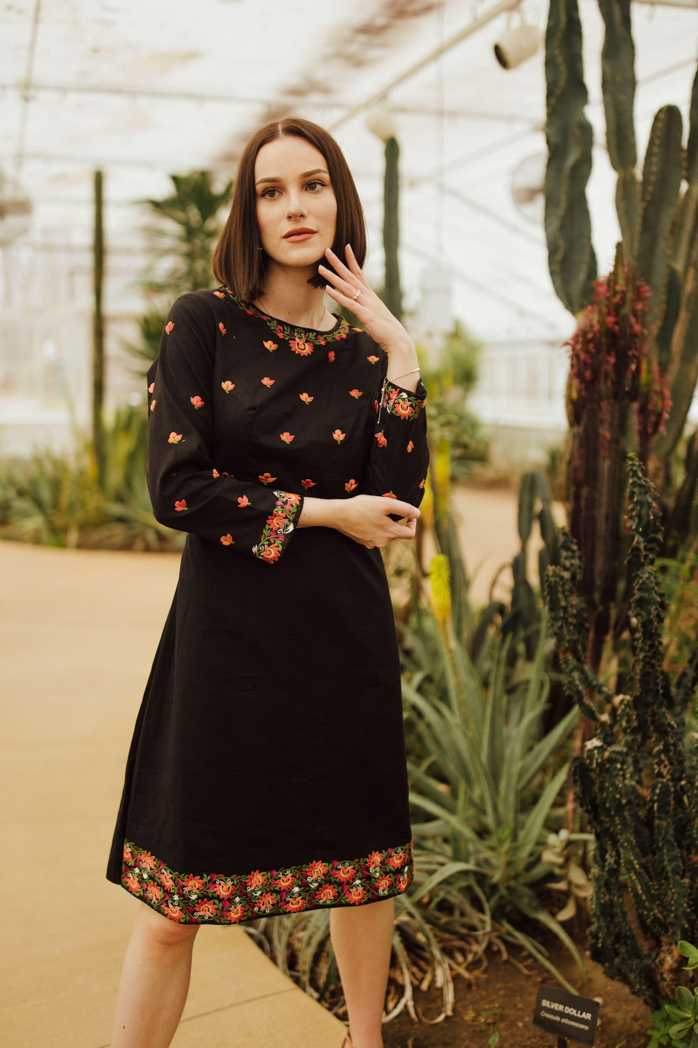 Black cotton midi dress with vibrant floral embroidery on neckline, sleeves, torso, and hem.