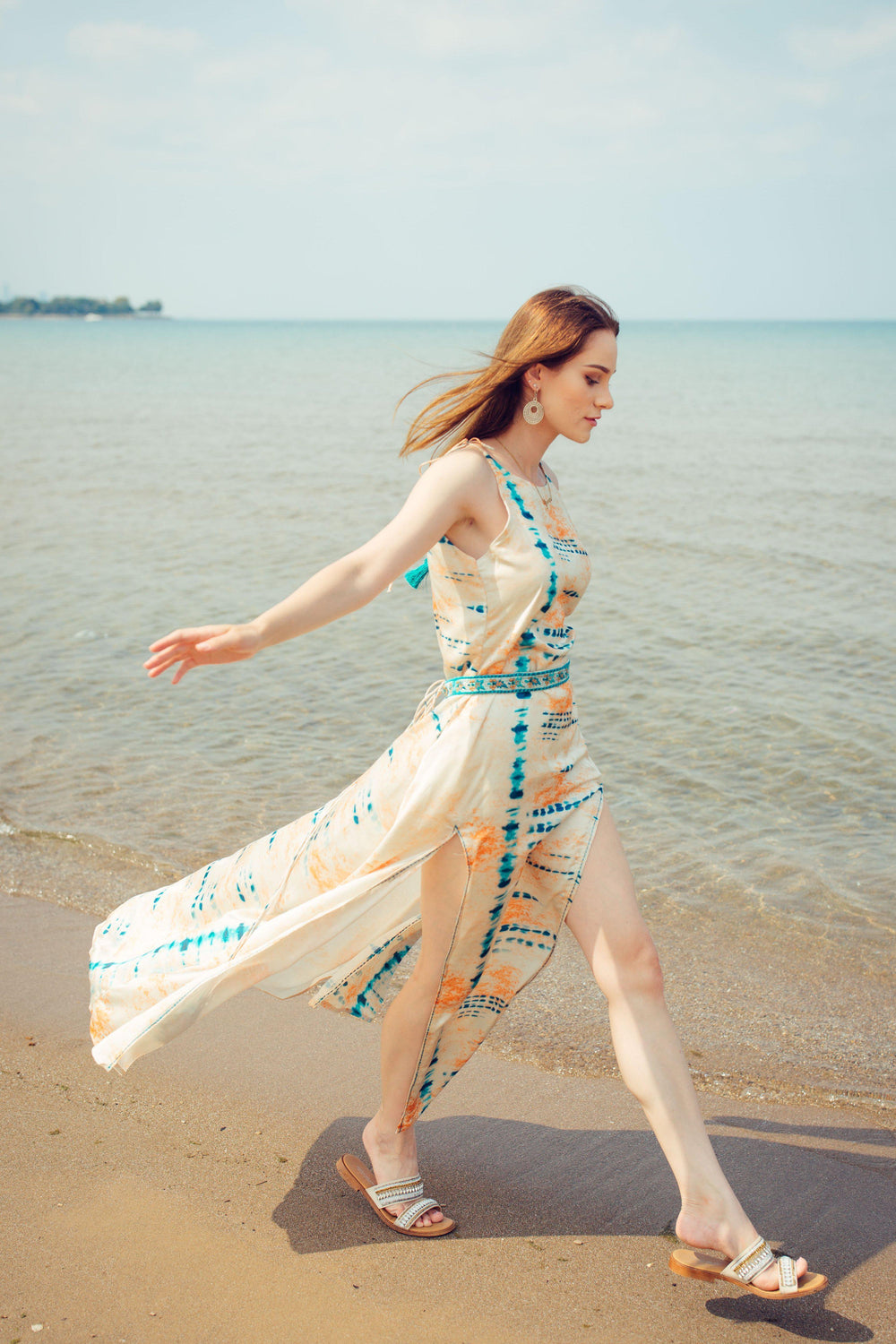 Off-white modal satin maxi dress with blue tie-dye, embroidered belt, and double slits, worn on a beach.