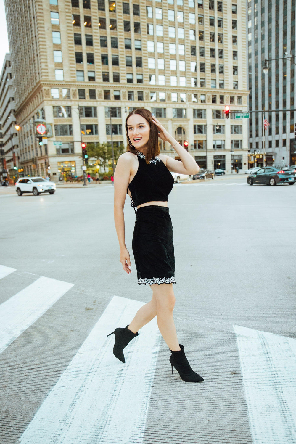 Woman in Luna black velvet embroidered crop-top and mini skirt set, walking on a city street.