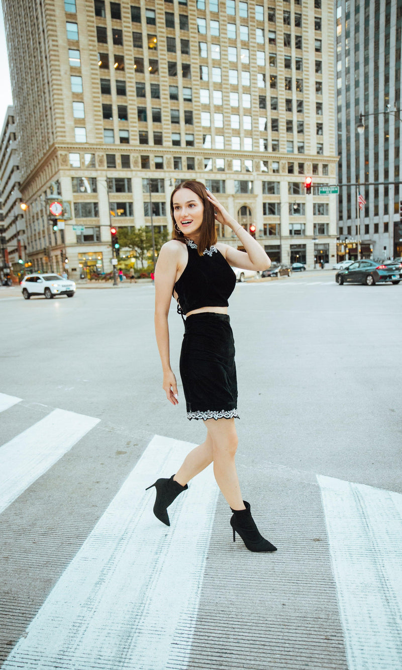Woman in Luna black velvet embroidered crop-top and mini skirt set, walking on a city street.