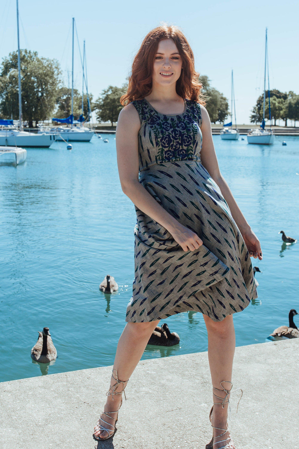 Grey cotton mini dress with intricate embroidery on the neckline and torso, worn by a model by a lake.