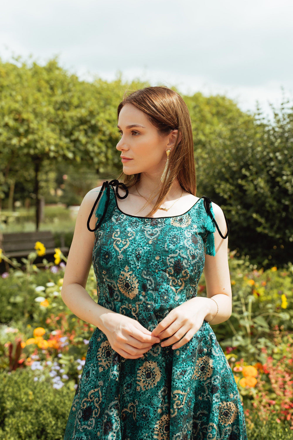 Teal blue silk mini dress with all-over eyelet embroidery, worn by a woman in a garden.