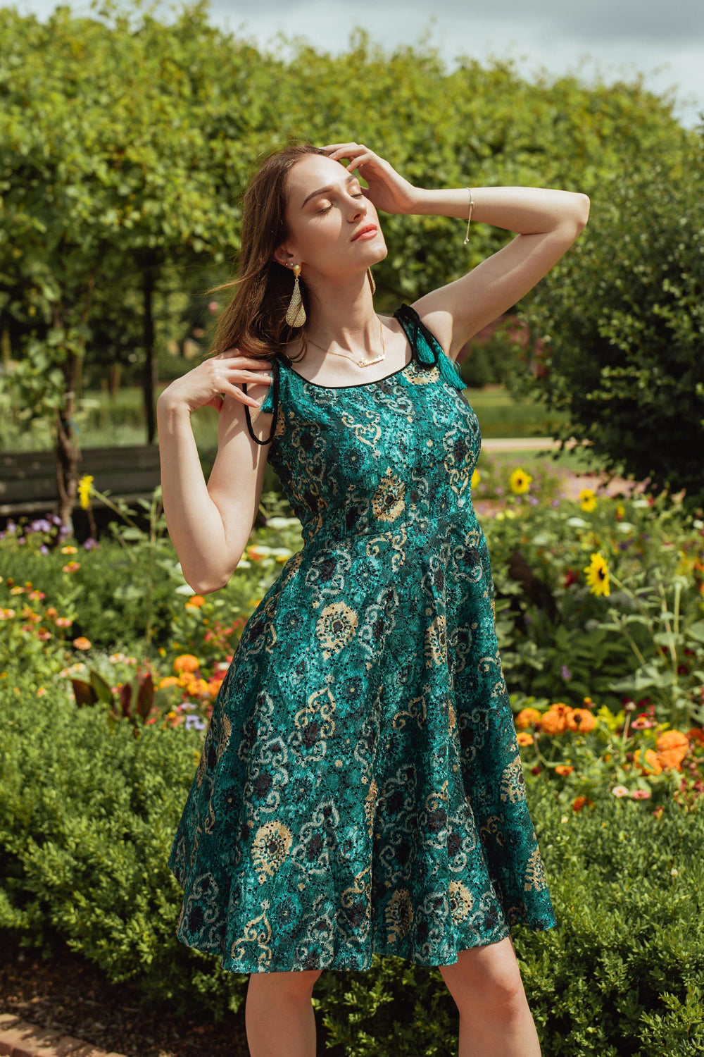 Teal blue silk mini dress with all-over eyelet embroidery, worn by a model in a garden.