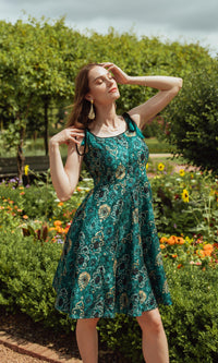 Teal blue silk mini dress with all-over eyelet embroidery, worn by a model in a garden.