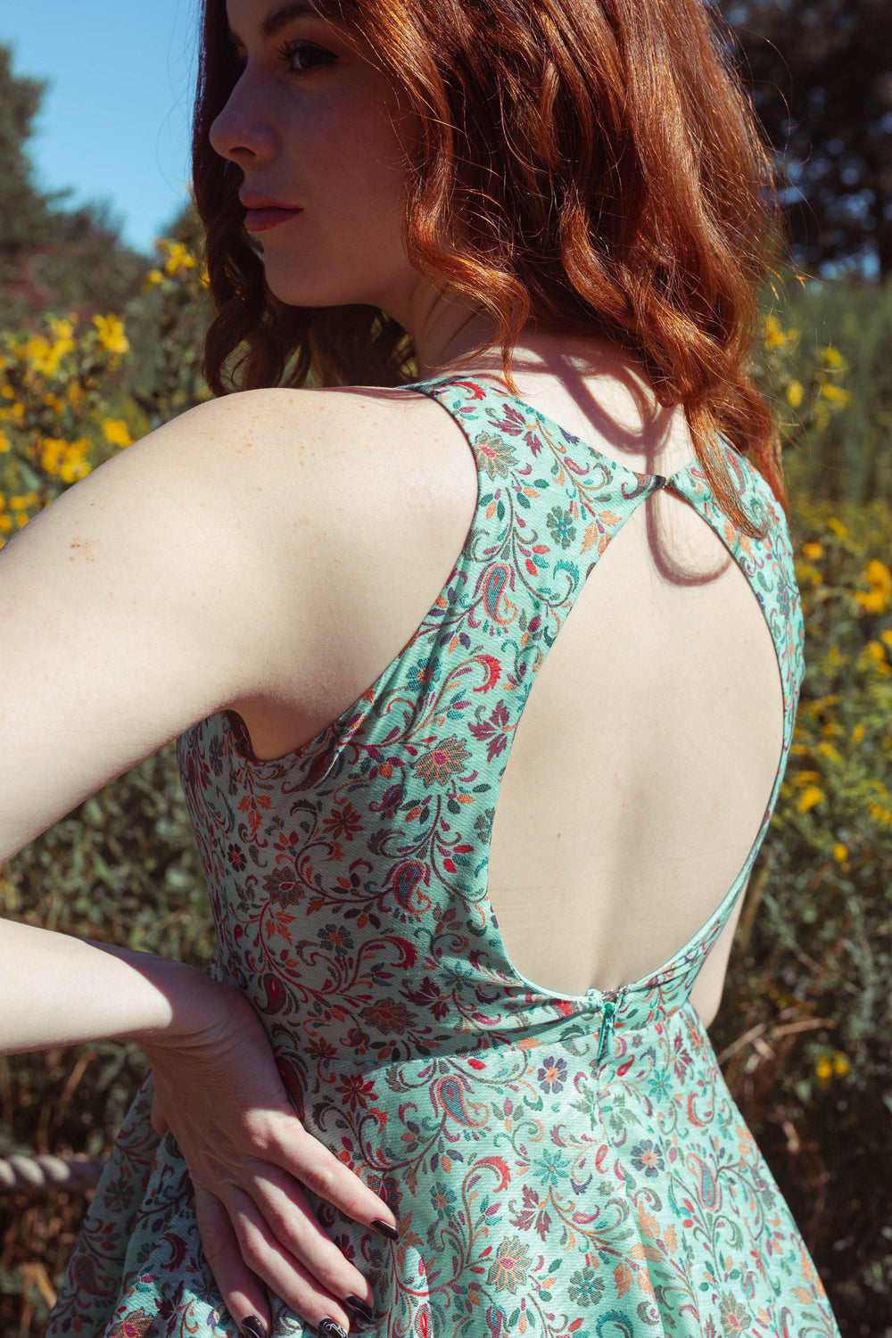 Woman in a green cotton-silk short dress with multicolor paisley patterns and a back keyhole cutout.