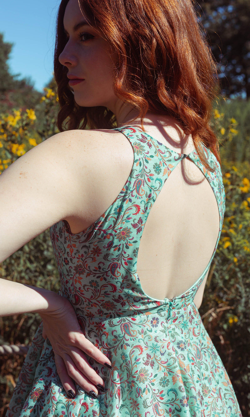 Woman in a green cotton-silk short dress with multicolor paisley patterns and a back keyhole cutout.