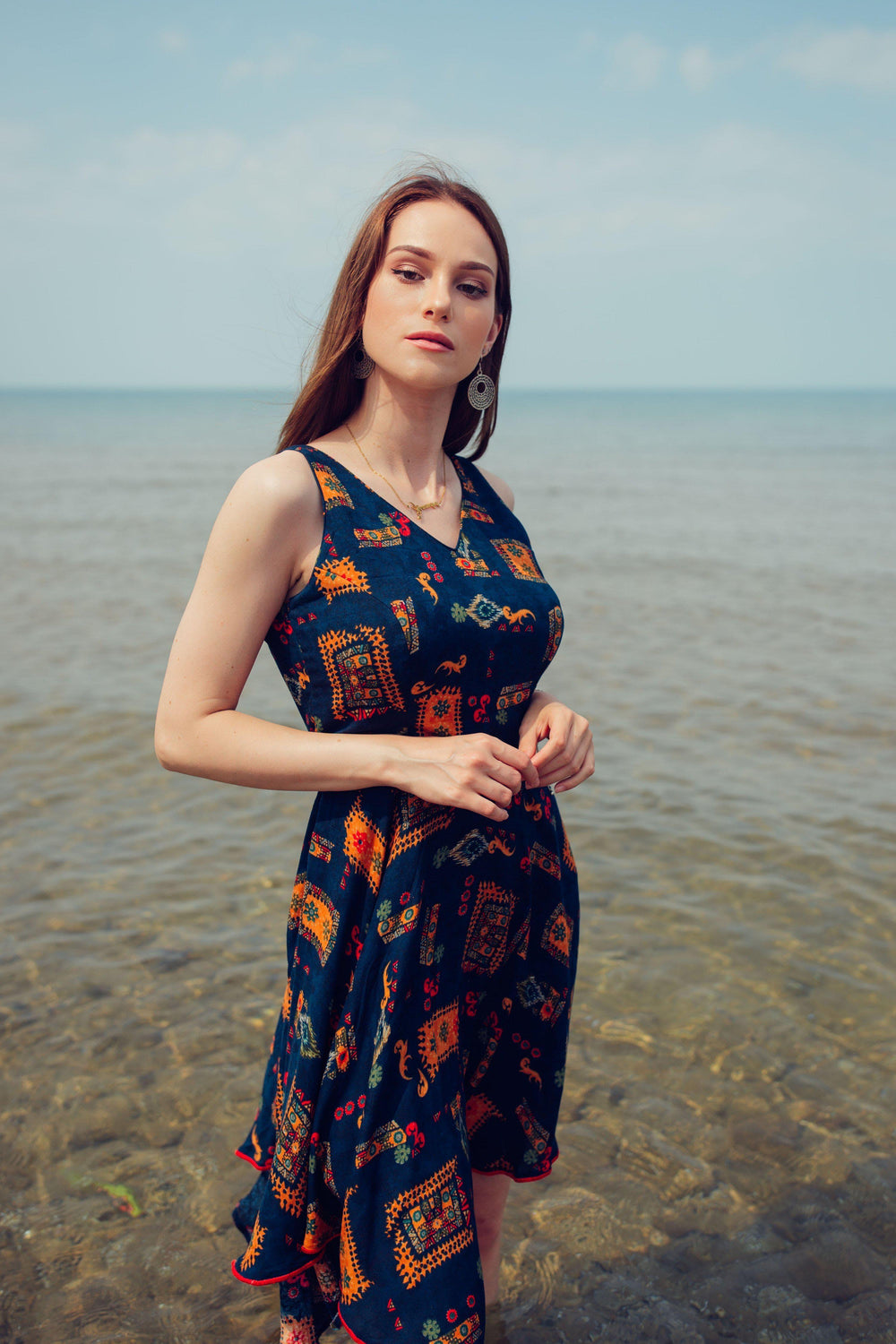 Woman in a navy rayon high-low dress with all-over patterns, V-neck, and sleeveless design, standing in water.