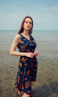 Woman in a navy rayon high-low dress with all-over patterns, V-neck, and sleeveless design, standing in water.