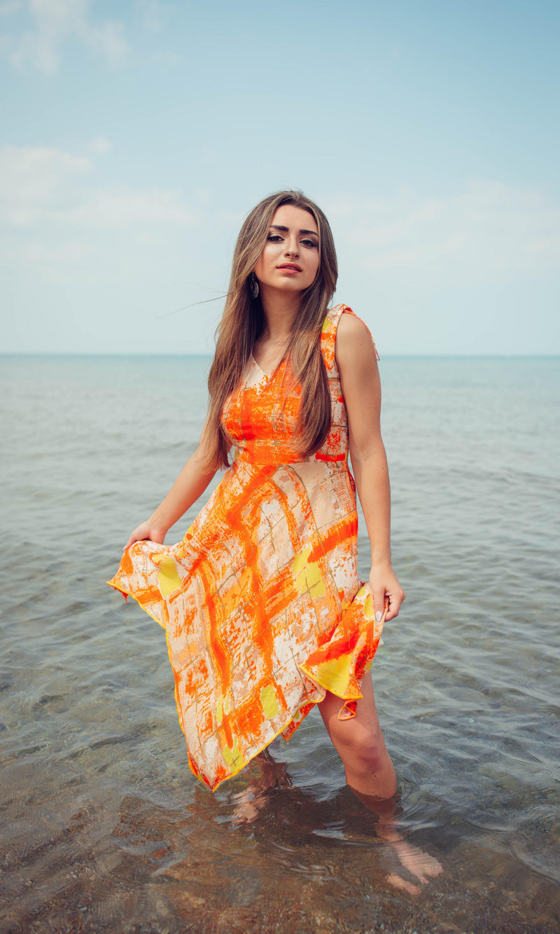 Woman in a vibrant orange tie-dye viscose rayon high-low dress, standing in shallow ocean water.