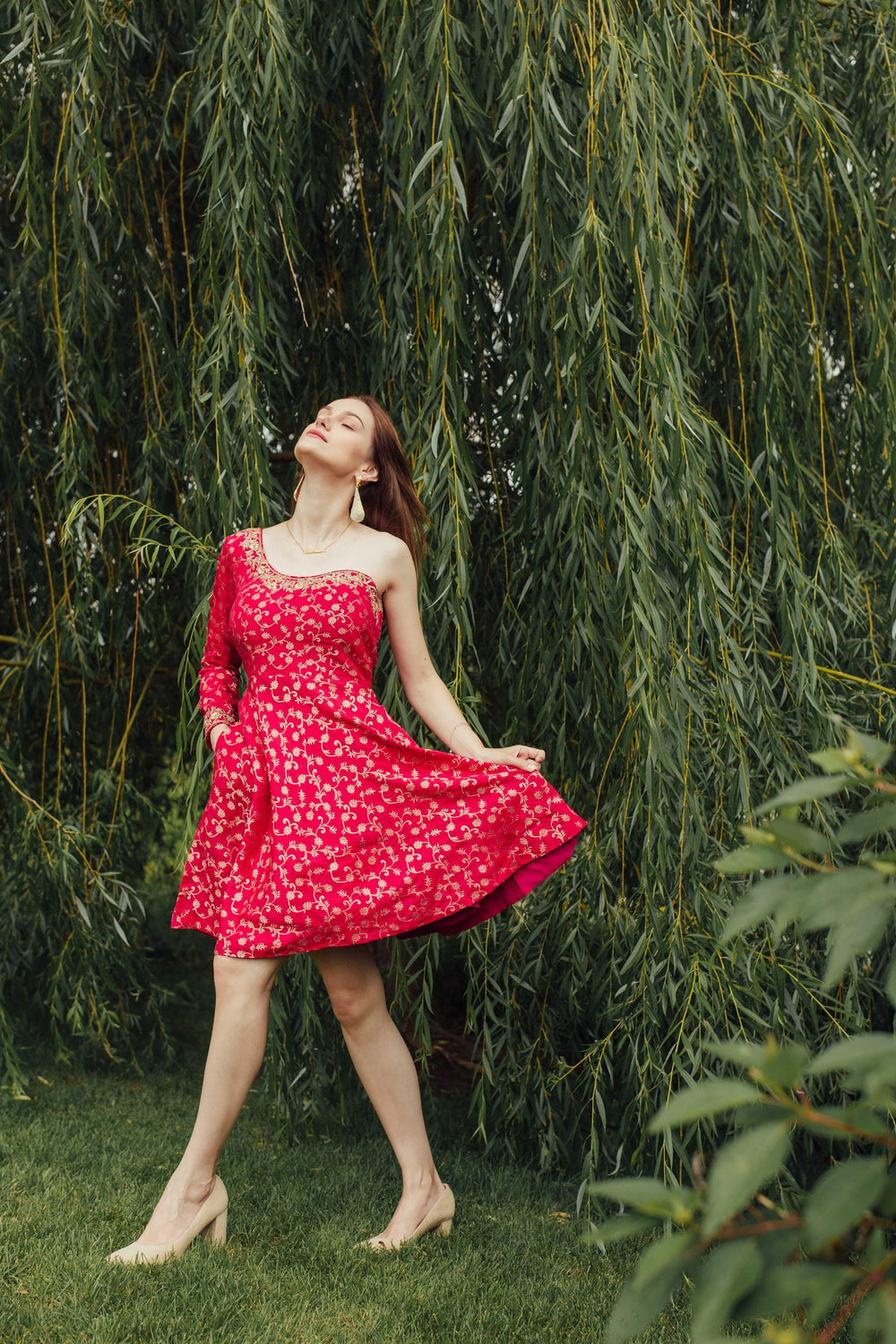 Dark pink silk one-shoulder mini dress with all-over golden hand embroidery, worn by a model outdoors.