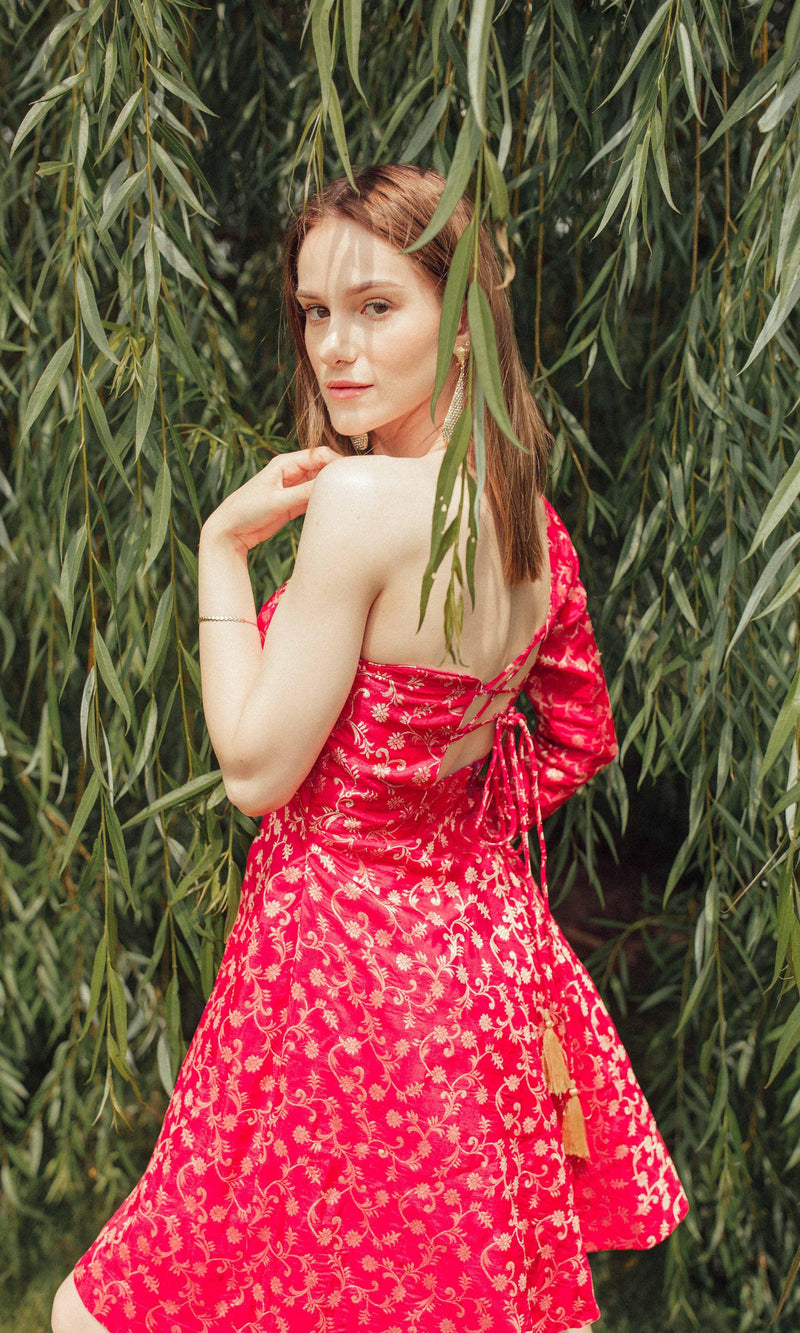 Dark pink silk one-shoulder mini dress with golden hand embroidery, worn by a model in nature.