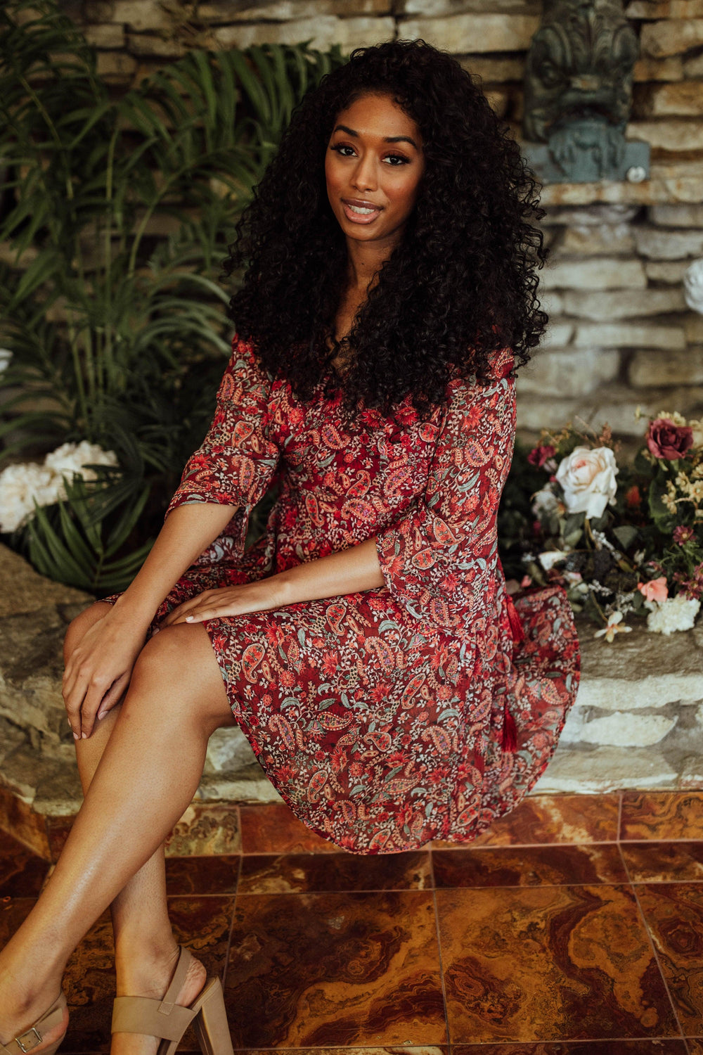 Woman in a red georgette mini dress with all-over print, V-neck, and 21" sleeves, sitting.