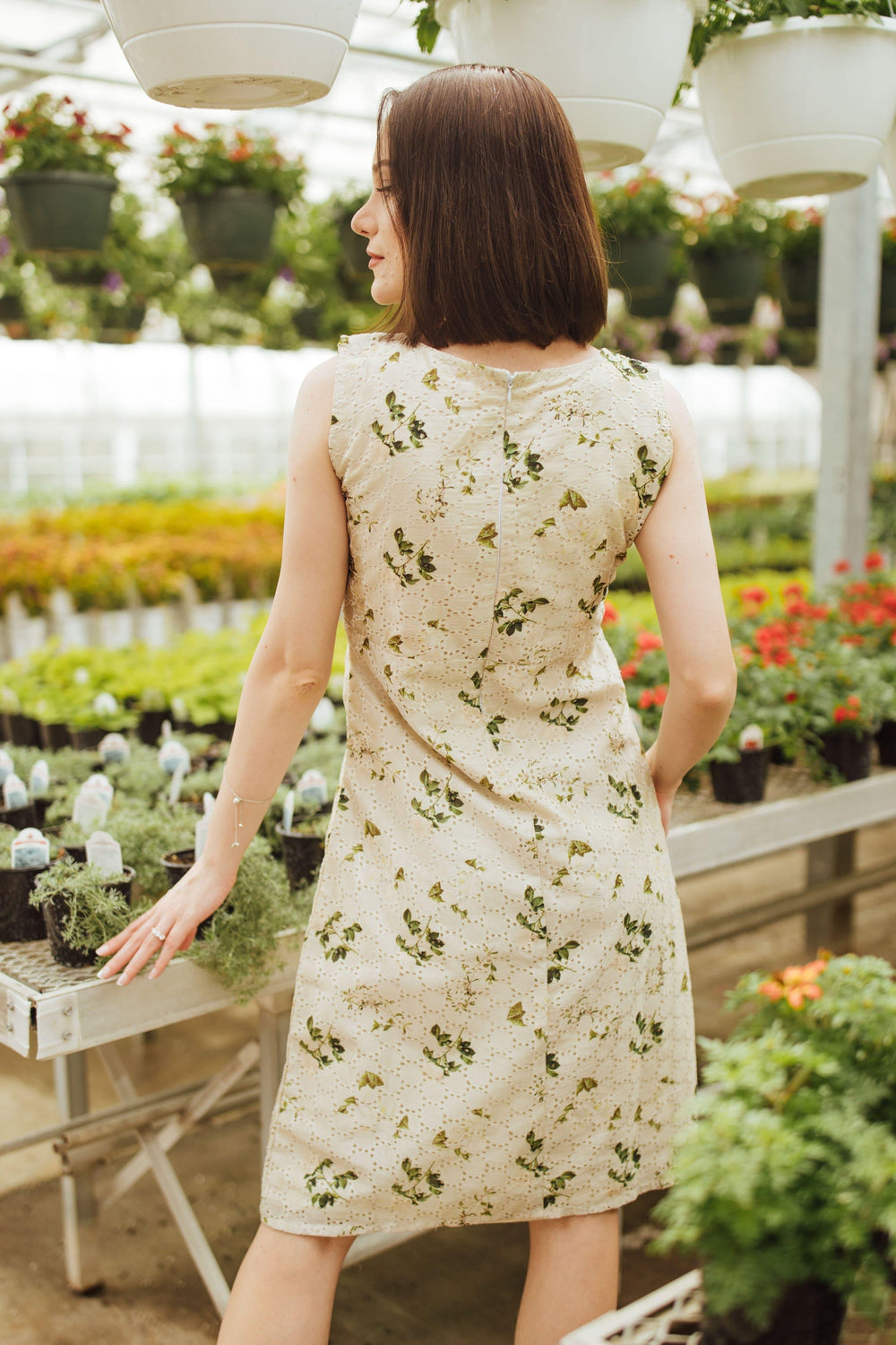 Woman in a sleeveless, off-white silk midi dress with all-over eyelet embroidery, viewed from the back.