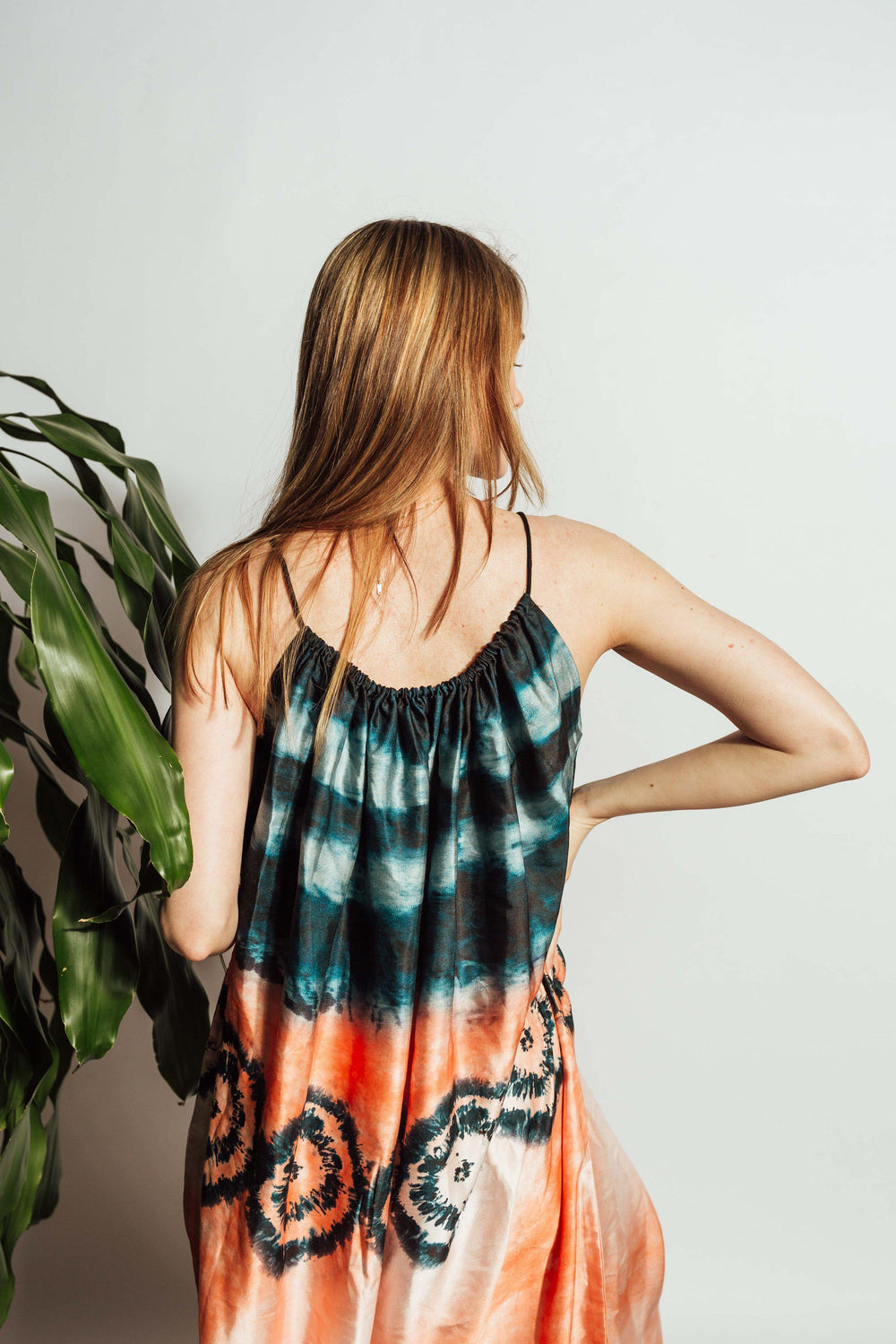 Back view of a woman wearing a silk tie-dye midi dress with teal, orange, and peach hues.