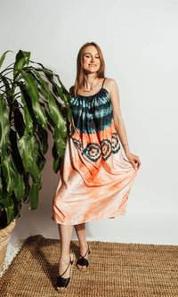 Silk tie-dye midi dress with teal bodice, peach hem, circular motifs, spaghetti straps, and gathered neckline.
