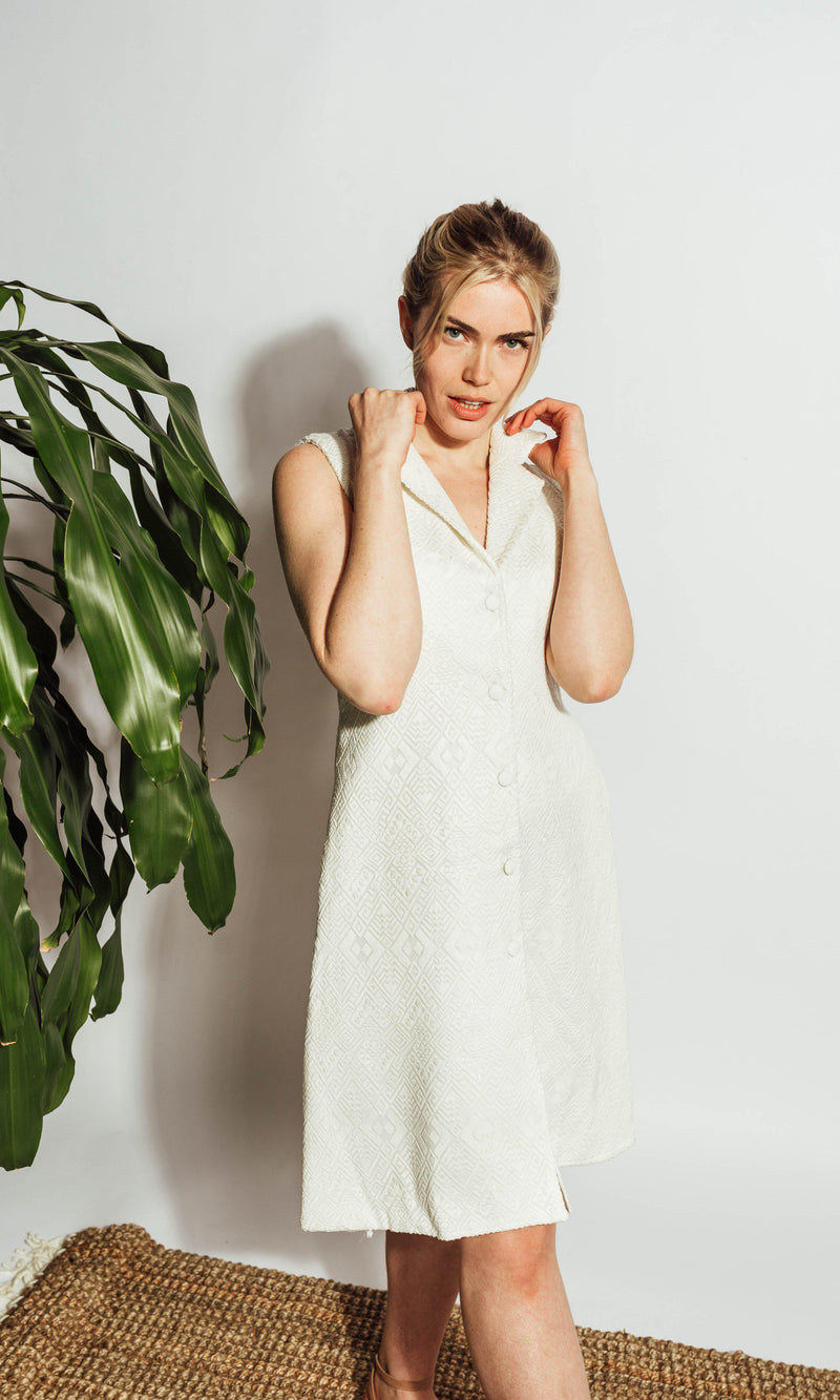 White sleeveless blazer dress with self-thread geometric embroidery, notched lapel, and front buttons.