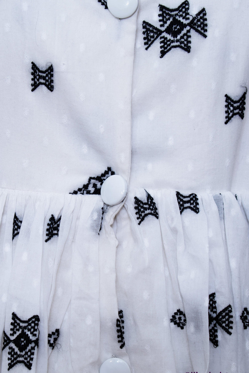 Close-up of a white mul cotton midi dress with black butta embroidery and front white buttons.