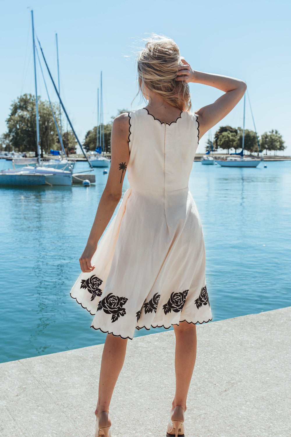White modal silk mini dress with black embroidered roses on the scalloped hem, worn by a woman outdoors.
