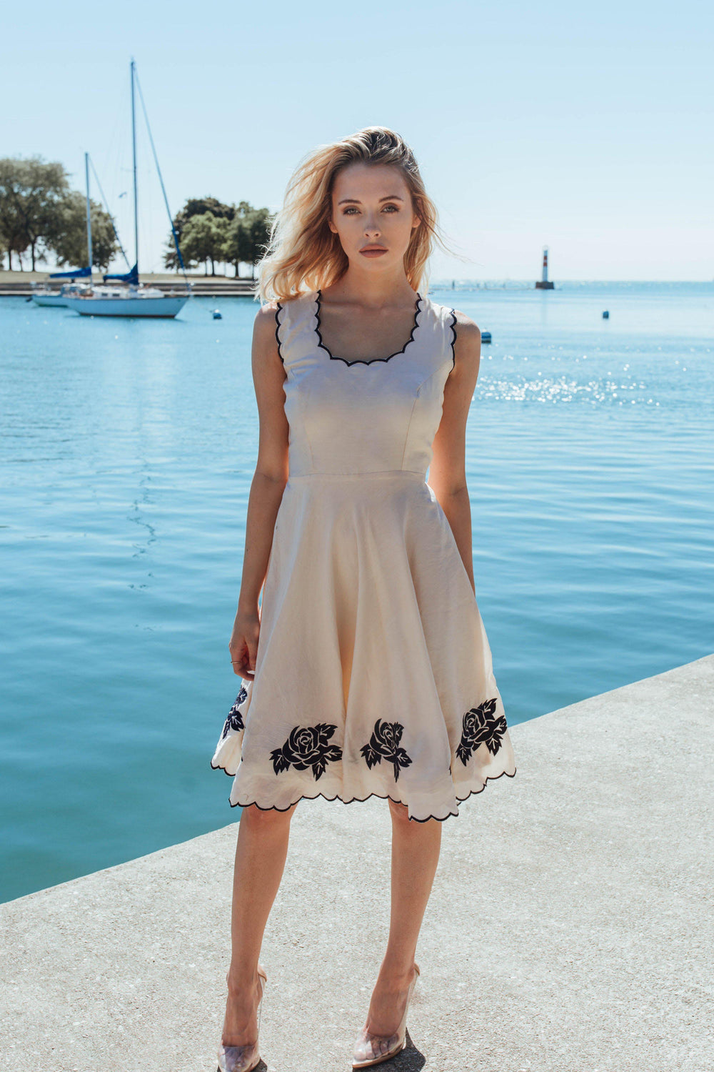 White sleeveless fit-and-flare mini dress with black floral embroidery on the hem and neckline.