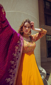 Yellow A-line hand-embroidered gown with multicolor resham work, paired with a magenta silk drape.